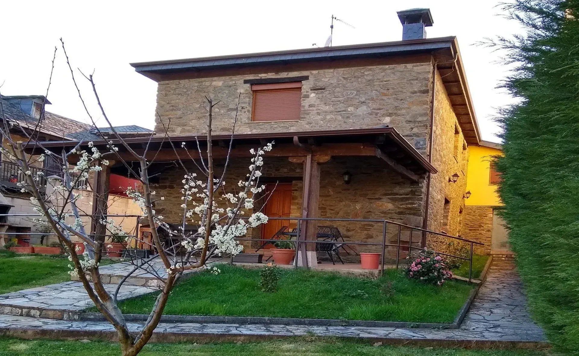 Fachada de piedra de la casa con un cerezo en flor en el jardín